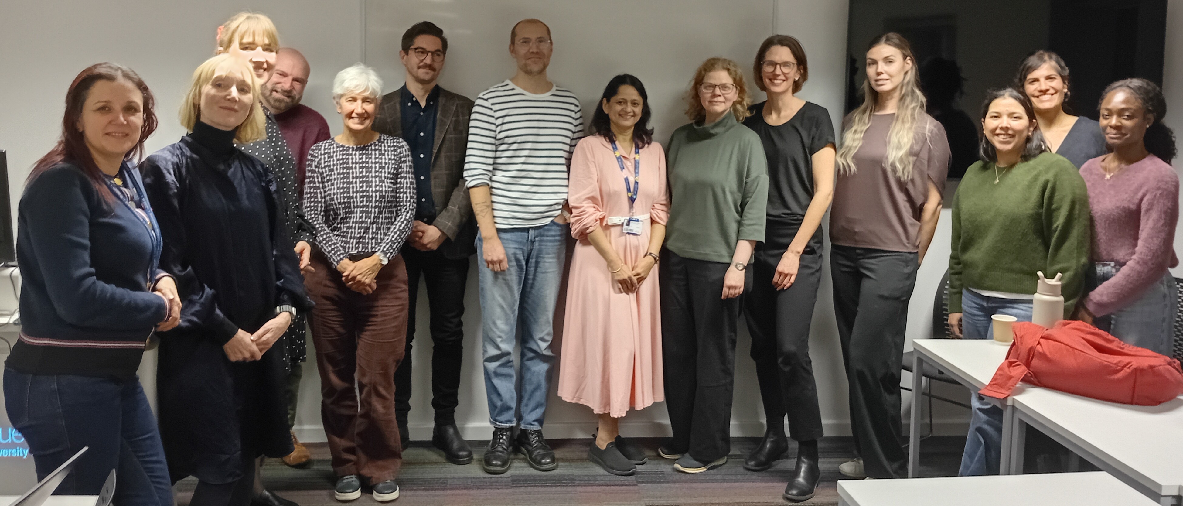 Image of a large group of researchers standing in a room smiling and dressed in smart casual wear