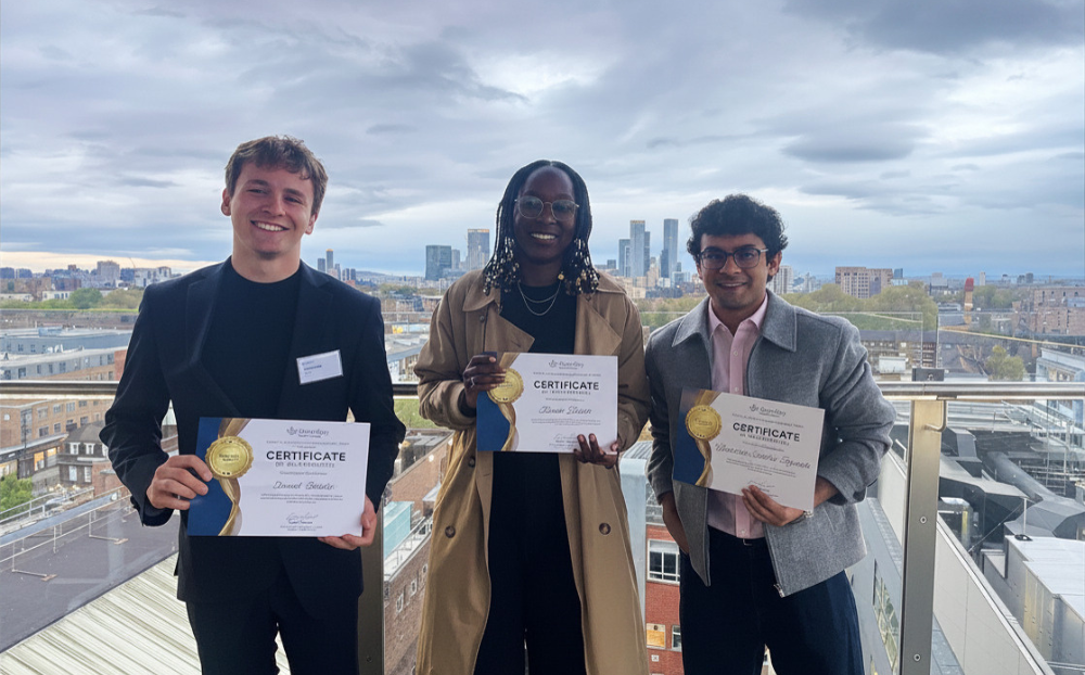 An image of three student mentees standing holding certificates in front of the london skyline