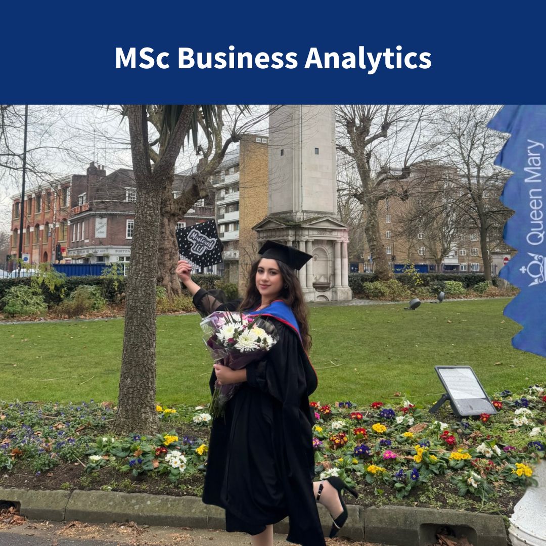 A student wearing a graduation gown carrying flowers and smiling infront of a clocktower at Queen Mary University of London