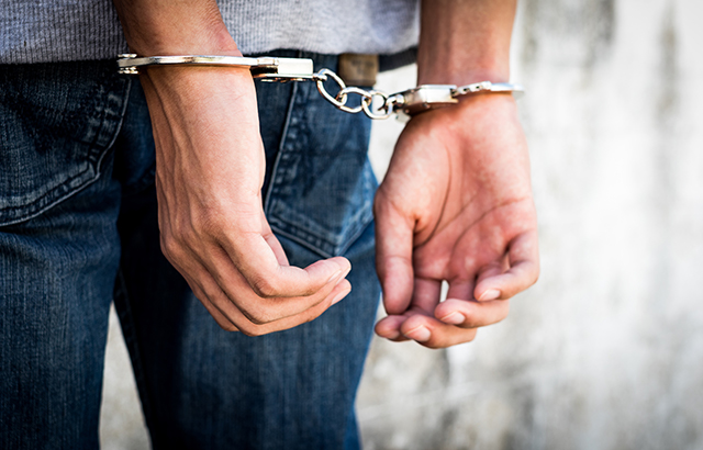Close up hands tied up handcuffs in behind his body. Arrested man handcuffed hands at the back.