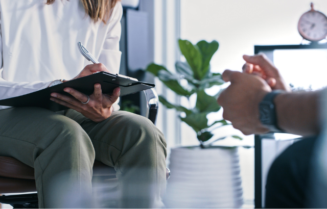 Female therapist writing notes while in session with a male patient.