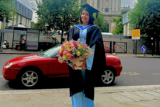 Student in graduation gown holding flowers looking at camera