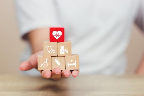 A person’s hand holding a stack of wooden blocks, featuring different healthcare-related icons, arranged in a pyramid.